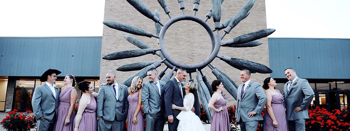 Photo of a wedding party with the bride, groom, and 5 bridesmaids and groomsmen in front of the sculpture outside the Brazos Center.